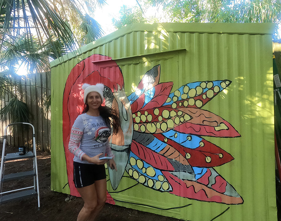 Patricia Filomeno painting a colorful pink flamingo mural on an outdoor shed in Sarasota, Florida