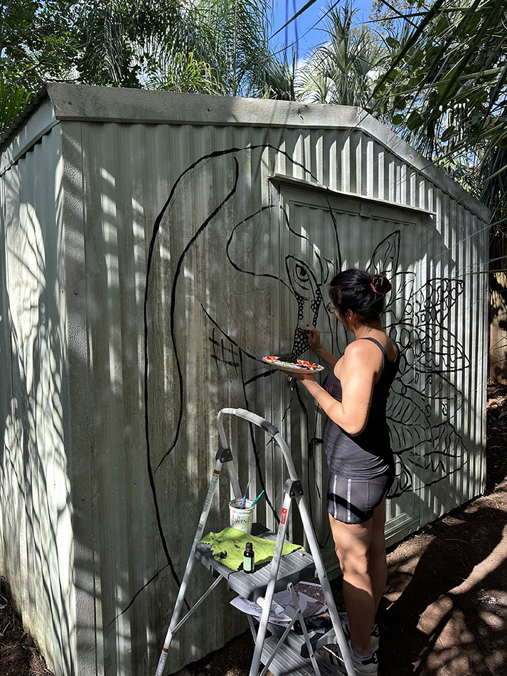 Patricia Filomeno painting a pink flamingo mural on a shed in Sarasota, Florida